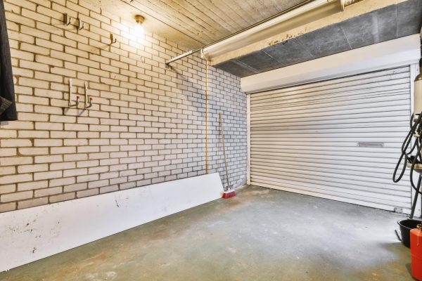 Spacious garage with closed white door and brick walls with hangers on it